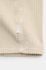 Nahaufnahme des sandfarbenen 04651/ A trip in a bag Cord-Overshirts, Detailansicht der Baumwoll-Cordstruktur und kleinem Weblabel an der Seitennaht.