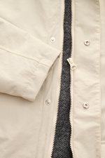 Nahaufnahme des Reißverschlusses und Ärmels des 04651/ A trip in a bag Parka "The Coat" sand aus hochwertiger Microfaser mit strukturierter Oberfläche.