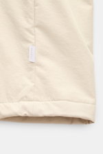 04651/ A trip in a bag Parka 'The Coat' sand in Nahaufnahme, Detail der Microfaser mit Logo-Weblabel und leicht strukturierter Oberfläche.