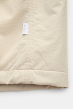 Nahaufnahme der unteren Kante der 04651/ A trip in a bag Jacke sand, hochwertige Microfaser mit glattem Griff, leichte Wattierung, Regular Fit, wind- und wasserabweisend, sichtbares Weblabel in der Seitennaht.