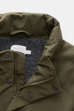 Nahaufnahme der olivgrünen 04651/ A trip in a bag Jacke oliv, von oben fotografiert, zeigt hochwertigen Microfaserstoff mit glattem Griff, Reißverschluss, Druckknöpfen, innen Woll-Mix-Futter, Raglanärmel und versteckte Kapuze im Kragen.