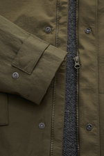 Nahaufnahme aus frontaler Perspektive der 04651/ A trip in a bag Jacke oliv mit hochwertiger Microfaser, glattem Griff, leichter Wattierung, wind- und wasserabweisend, Regular Fit, Reißverschluss, versteckter Kapuze im Kragen, Raglanärmeln, Hüfttaschen mi