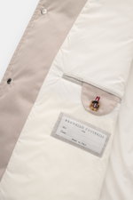 Innenansicht der Brunello Cucinelli Jacke sand, Detailaufnahme mit geschmeidigem Futter, Innentasche mit Knopf und Markenlabel „Made in Italy“.