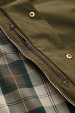 Nahaufnahme der Barbour Wachsjacke 'Icons Border Casual' oliv von innen mit typisch kariertem Tartan-Futter, Reißverschluss und goldfarbenen Druckknöpfen.