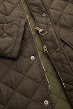 Barbour Steppjacke 'Chelsea Sportsquilt' oliv, Nahaufnahme von Fronttasche, Zwei-Wege-Reißverschluss und Steppmuster aus schräger Perspektive.