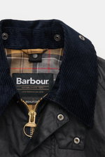 Close-up front view of Barbour Waxed jacket 'Beaufort' dark navy showing waxed cotton, corduroy collar, gold zipper, and classic tartan lining.

<p>A true classic in the British outdoor tradition: The waxed jacket 'Beaufort' by BARBOUR is made of robust, 