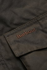 Nahaufnahme der Fronttasche mit Barbour-Logo aus Leder der Barbour Wachsjacke 'Sander' dark olive aus gewachster Baumwolle, wasserabweisend.