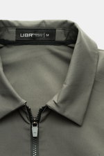 Nahaufnahme der UBR Jacke 'Nano' graugrün von oben frontal, zeigt glatten Microfaserstoff, Umlegekragen und zwei-Wege-Reißverschluss, wind- und wasserabweisend, slim fit, elastische Ärmelabschlüsse, reflektierender Logo-Print.