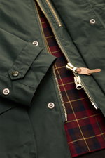 Close-up front view of the Manifattura Ceccarelli Waxed jacket 'Raincaban' dark green, showing paraffin-treated waxed cotton fabric, gold two-way zipper with leather pull, snap buttons, cuff with button, and iconic tartan lining. Authentic outerwear with 