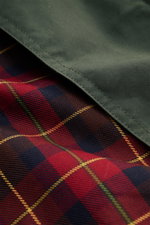 Close-up from an angled top view showing the dark green waxed cotton exterior and red tartan lining of the Manifattura Ceccarelli Waxed jacket 'Raincaban' dark green, authentic Italian outerwear with paraffin-treated, water repellent cotton fabric and ico