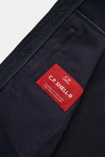 Nahaufnahme der Innenseite der navy C.P. Company Softshell-Jacke "C.P. Shell-R Goggle Jacket" mit rotem Label und Softshell-Material aus recycelter Microfaser.