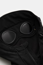 Nahaufnahme von der Kapuze der C.P. Company Softshell-Jacke 'C.P. Shell-R Goggle Jacket' schwarz, Softshell aus recycelter Microfaser mit Goggle Lenses, weicher Griff, Slim Fit, wind- und wasserabweisend, von oben fotografiert.