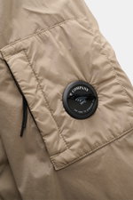 Nahaufnahme des Ärmels mit Logodetail und Tasche des graugrünen C.P. Company Blouson aus recycelter Microfaser, Slim Fit, garment dyed, mit elastischem Bündchen.