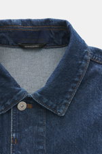 Nahaufnahme der Stone Island Jeansjacke 'Indigo Denim-Rinsed' dunkelblau, Slim Fit mit Umlegekragen und verdeckter Knopfleiste, fotografiert von vorne oben.