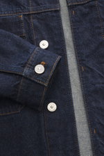 Close-up front view of Stone Island Denim jacket 'Indigo Denim-Rinsed' dark blue showing indigo cotton fabric, concealed button placket, and cuff with Stone Island branded buttons.