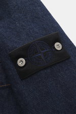 Close-up side view of Stone Island Denim jacket 'Indigo Denim-Rinsed' dark blue, showing indigo-dyed cotton texture and black compass badge with metal buttons. For casual denim looks: This denim jacket in indigo-dyed cotton yarn from the 'Denim' capsule c