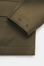 Close-up front-side view of Stone Island Jacket 'Panno Ghost Piece' olive showing buttoned sleeve cuff, mix of wool and microfiber, textured feel, slim fit, five-button placket, patch chest pockets, front pockets with flap, turn-down collar, tonal compass