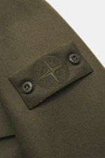 Close-up view of the sleeve of the Stone Island Jacket 'Panno Ghost Piece' olive, showing its mix of wool and microfiber, textured feel, tonal compass badge with buttoned flap, and smooth lining fabric. The slim fit jacket features a five-button placket, 
