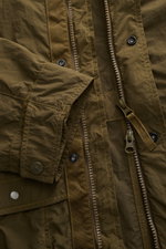 Nahaufnahme der Stone Island Jacke 'Nylon Smerigliato Ghost Piece' oliv, seitlich fotografiert, zeigt Reißverschluss, Knöpfe und Mikrofasermaterial.