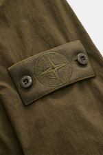 Stone Island Jacke 'Nylon Smerigliato Ghost Piece' oliv Detailaufnahme des Kompass-Badges auf rauer Microfaser, Perspektive nah und schräg.