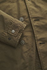 Nahaufnahme der Stone Island Jacke 'David-TC Ghost Piece' oliv von schräg oben, zeigt Knopfleiste und verstellbaren Ärmel mit Ton-in-Ton-Badge.