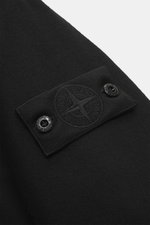 Close-up view of the tonal badge on the upper arm of the Stone Island Blouson 'Wool Nylon Flannel Ghost Piece' black, made from a mix of virgin wool and microfiber with a soft feel, slim fit, six-button placket, turn-down collar, buttoned sleeve cuffs, qu
