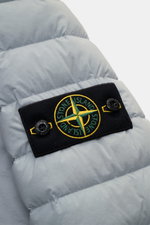 Stone Island Daunenjacke 'Seamless Tunnel Nylon Down-TC' rauchblau close-up of padded fabric and black compass badge with buttons, shown from back. <p>Die Jacke 'Seamless Tunnel Nylon Down-TC' von STONE ISLAND überzeugt mit innovativer Verarbeitung, leich