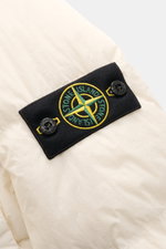 Stone Island Down jacket 'Garment Dyed Crinkle Reps NY' cream close-up from side shows black logo patch with green-yellow compass and buttons on crinkle microfiber fabric. Innovative coated material in a signature garment-dyed look meets modern outdoor st