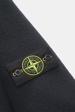 Nahaufnahme der Stone Island Jacke 'Heavy Melton' navy im Dufflecoat-Stil, Fokus auf das Kompass-Badge aus Wolle-Kaschmir-Gewebe mit Knöpfen.