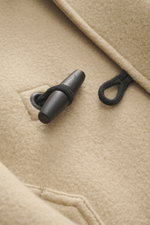 Nahaufnahme eines Knebelverschlusses der Stone Island Jacke 'Heavy Melton' beige aus Wolle und Kaschmir, Detailansicht des dufflecoat-stils.