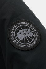 Nahaufnahme des tonalen Weblabels auf dem linken Ärmel des Canada Goose Daunenparka 'Langford' schwarz, gefertigt aus glattem Arctic-Tech-Material.