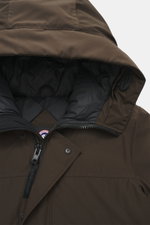 Close-up front view of Canada Goose Down parka 'Langford' dark brown with hood, zipper, and snap buttons, showcasing smooth Arctic-Tech fabric. Urban style with an arctic background – the down parka 'Langford' by CANADA GOOSE impresses with its clear, fun