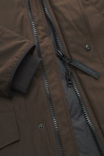 Close-up shot of the Canada Goose Down parka 'Langford' dark brown, showing the two-way zipper, snap button storm flap, and ribbed windbreaker cuff. Urban style with an arctic background – the down parka 'Langford' by CANADA GOOSE impresses with its clear