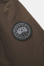 Canada Goose Down parka 'Langford' dark brown close-up of upper sleeve with black Arctic Program patch, front side view. Urban style with an arctic background – the down parka 'Langford' by CANADA GOOSE impresses with its clear, functional design and prot