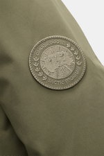 Close-up of the tonal woven label on the sleeve of the Canada Goose Down parka 'Langford' grey green, photographed from the side. Urban style with an arctic background – the down parka 'Langford' by CANADA GOOSE impresses with its clear, functional design