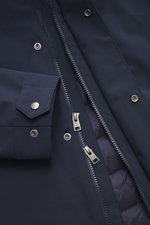 Close-up front view of Woolrich Softshell down jacket 'Barrow' dark blue showing water-repellent softshell made of elastic microfiber with smooth feel, two-way zipper, snap buttons on wind flap, adjustable sleeve cuffs, quilted lining fabric, and hand war