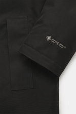 Close-up front-side view of Woolrich Down jacket 'Heavy GTX' black sleeve showing GORE-TEX logo, high-quality microfiber, wind- and water-repellent, warm down filling, slim fit, robust two-way zipper, wind flap with buttons, high-closing collar with hood,
