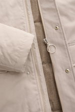 Close-up front view of the 04651/ A trip in a bag Parka 'MC26' sand, showing the sand-colored lightly waxed cotton fabric, two-way zipper with large ring pull, snap buttons, and warm wool-mix lining. <p>Inspiriert von den Olympischen Winterspielen in Cort