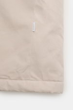 Close-up view of the hem and side seam of the 04651/ A trip in a bag Parka 'MC26' sand, made from lightly waxed cotton with a soft touch, featuring a small white fabric label with "04651" printed on it. Inspiriert von den Olympischen Winterspielen in Cort