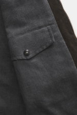 Close-up view of the left sleeve of the Belstaff Waxed jacket 'Trialmaster Phoenix' dark brown, showing the waxed cotton fabric, patch pocket with a black BELSTAFF snap button, and brown corduroy inner lining with zipper edge. Durable, functional and time
