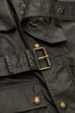 Nahaufnahme der Belstaff Wachsjacke 'Trialmaster' dark olive in gewachster, wasserabweisender Baumwolle, Fokus auf Taillengürtel, Druckknöpfe und Taschen.