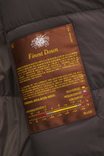 Close-up front view of the Moorer Down blouson 'Donizetti' grey melange showing the brown label with finest down details and thermal insulation index. High performance at temperatures from above freezing to below zero: The knitted down blouson 'Donizetti'