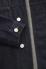 Close-up front detail of Stone Island Denim jacket 'Indigo Denim-Raw' navy showing raw denim fabric, orange stitching, silver branded buttons, and cuffs with button from a top-down perspective.