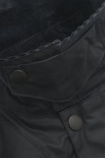 Close-up image from above of the collar and upper chest area of the Barbour Wachsjacke 'Reelin Wax' dark olive, showcasing the waxed cotton material, corduroy collar, and branded snap buttons. The jacket features a classic British countryside style with w