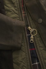 Nahaufnahme aus seitlicher Perspektive der Barbour Wachsjacke 'Ogston' khaki mit gewachster Baumwolle, Reißverschluss, Druckknöpfen und charakteristischem Tartan-Futter.