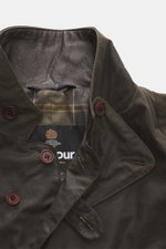 Close-up front view of the Barbour Wax Jacket 'Beacon' Dark Brown, showing the slim fit waxed cotton fabric, leather-trimmed adjustable collar, three-button placket, patch pockets, removable button strap, and characteristic tartan lining. British style ma