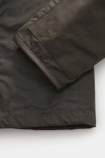 Barbour Wax Jacket 'Beacon' Dark Brown close-up from the sleeve perspective, showing waxed cotton, slim fit, leather trim, and patch pocket. British style materialises in the 'Beacon' model from BARBOUR: With a slim cut and leather trim on the collar, it 