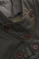 Close-up from above of the Barbour Wax Jacket 'Beacon' Dark Brown showing waxed cotton fabric, cowhide leather collar trim, button strap, and tartan lining. British style materialises in the 'Beacon' model from BARBOUR: With a slim cut and leather trim on