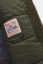 Nahaufnahme des Innenfutters vom Barbour Wachsparka 'Northfield Waterproof' dark olive mit Tartan-Label und gesteppter Wattierung, Detailansicht von innen.