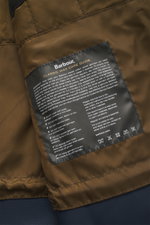 Close-up interior view of the Barbour Wax parka 'Ursula' dark navy showing the quilted lining and a black care guide label, highlighting waxed cotton, typical material texture, water-repellent, breathable fabric, double front, regular fit, robust two-way 